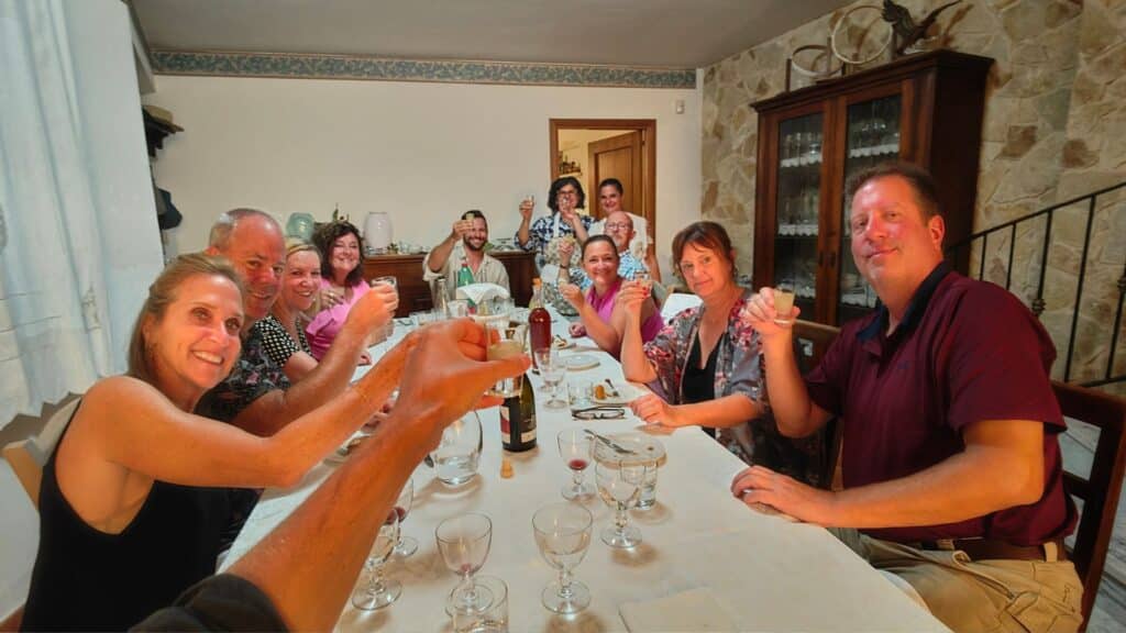 A group of people enjoying a traditional Sicilian meal in a private home on Mt. Etna, all raising their glasses for a toast around a large dining table