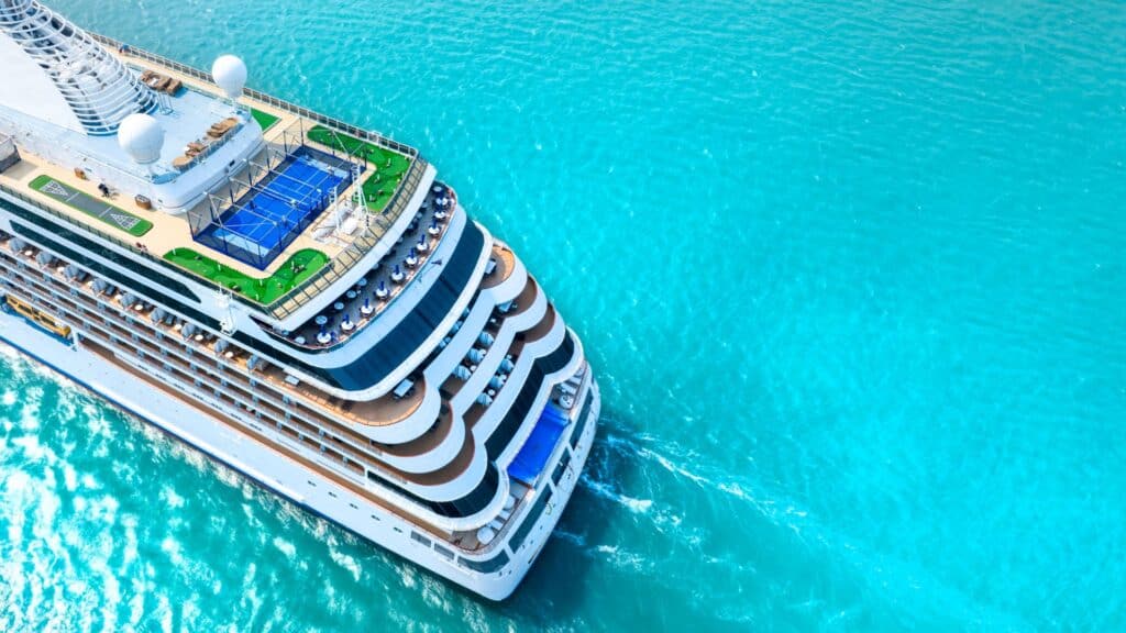 Aerial view of a large cruise ship sailing through turquoise waters, illustrating the environmental and cultural impact of mass tourism on popular destinations.