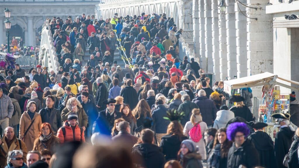 Crowds of tourists in Venice overwhelming a historic bridge, highlighting the economic and cultural impact of mass tourism on local communities.