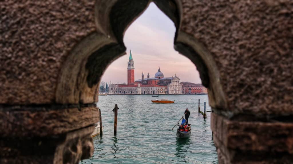 Discover Venice: A gondola on the Venetian lagoon with a view of San Giorgio Maggiore, framed by an ornate stone window.