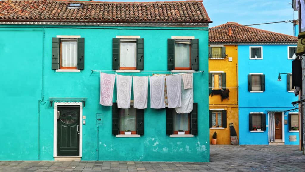 Colorful houses in Burano, Italy, with a vibrant turquoise facade and laundry hanging on a line, representing the island's iconic charm.