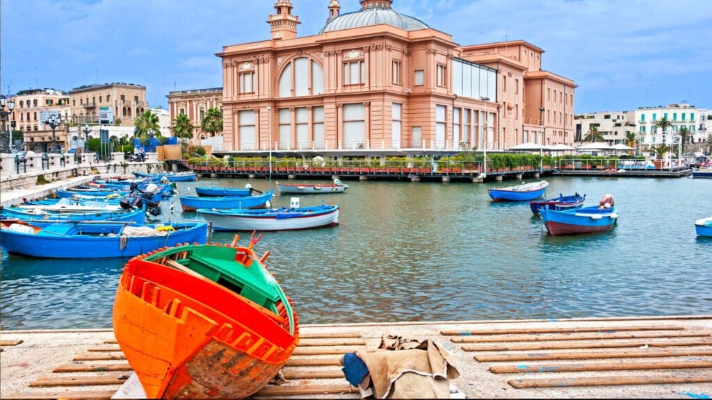 Colorful fishing boats docked near the historic Teatro Margherita in Bari, Puglia, Italy.