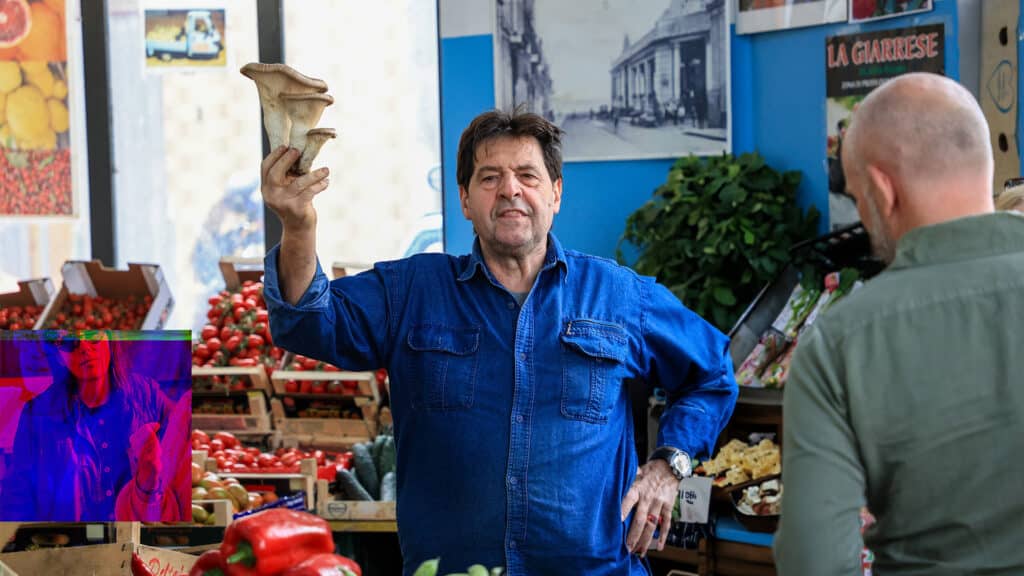 Sicilian merchant at Riposto market surrounded by fresh fruit, embodying Sensorial Travel™