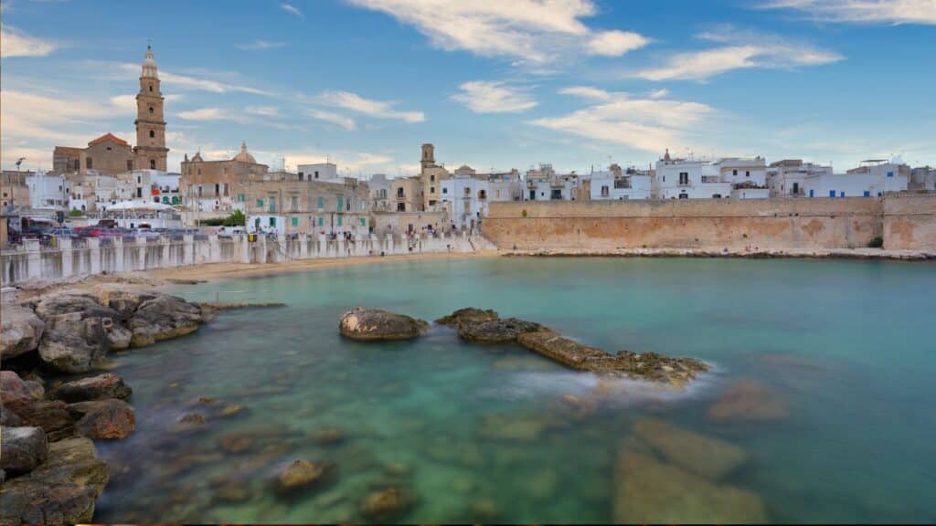 View of Monopoli’s waterfront with its historic buildings and the Mediterranean Sea, showcasing the balance between local life and cultural tourism in Puglia, Italy.