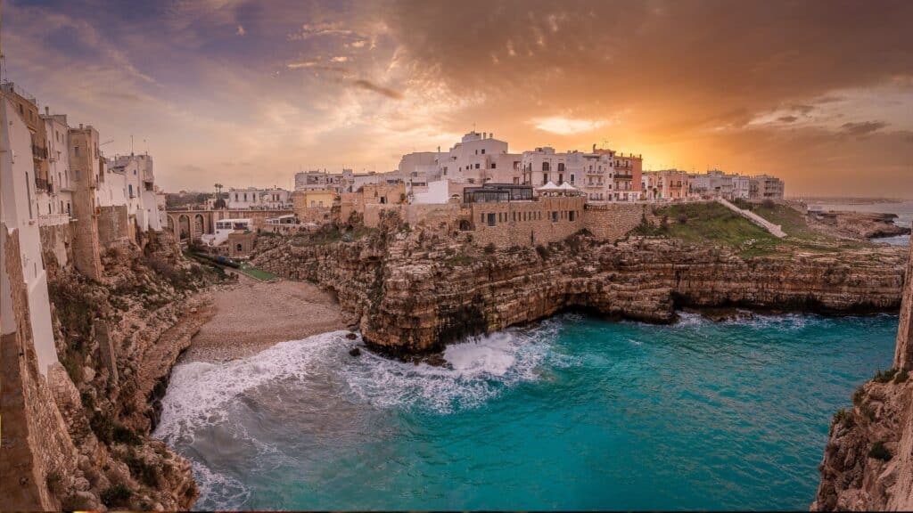 Polignano a Mare perched on limestone cliffs at sunset, overlooking the Adriatic Sea and famous for its caves and pristine beach, Lama Monachile.