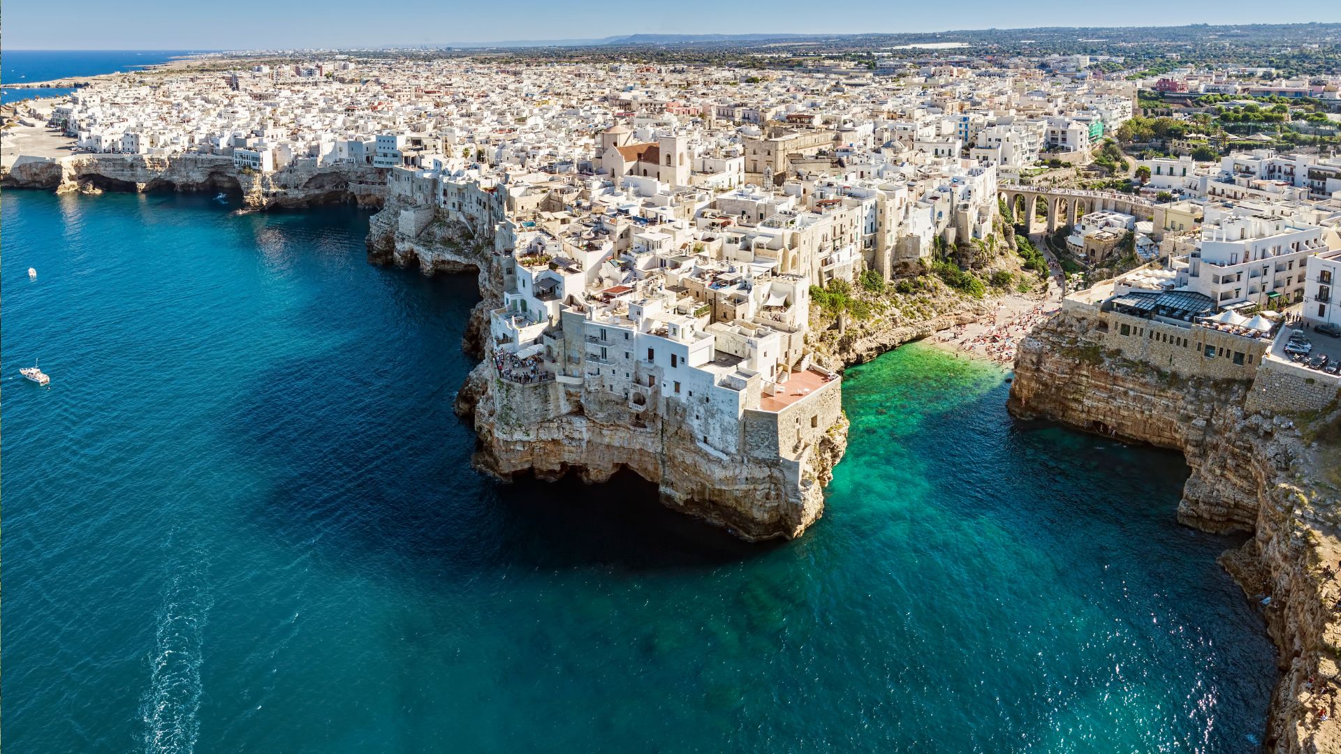 Aerial view of Polignano a Mare, a coastal town in Puglia, Italy, where whitewashed buildings perch on cliffs overlooking the Adriatic Sea, inviting you to travel to Puglia.