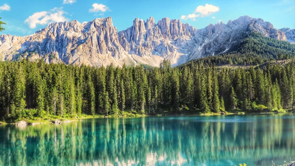 Scenic View Of Lake Carezza Surrounded By Lush Pine Forests And The Dolomite Mountains, Showcasing Italy’s Natural Beauty.