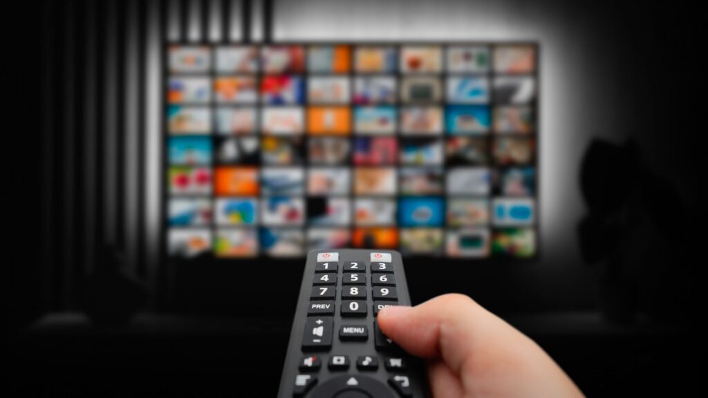 A Hand Holding A Remote Control Pointed At A Tv Screen, Ready To Stream Movies And Tv Shows Set In Iconic Italian Locations.