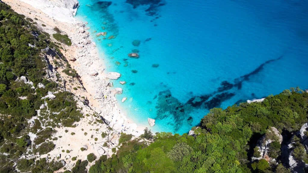 Aerial view of the Sardinian coastline overlooking turquoise waters, representing the seafood and coastal flavors of traditional Sardinian cuisine